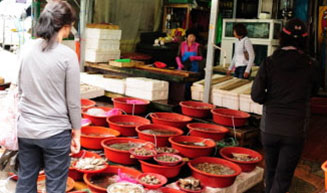 쌍봉시장의 한 수산가게에서 물건을 구매하려는 구매자들과 뒤로 보이는 수산물들이 가득담긴 좌판대들