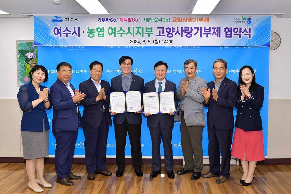 여수시 농협 여수시지부에서 고향사랑기부제 협약식이 진행되고 있으며, 여러 관계자들이 협약서를 들고 기념사진을 찍고 있다.