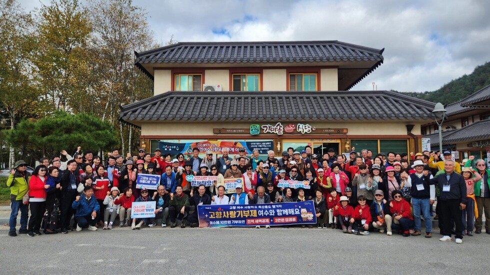 강원도 평창 오대산에서 열린 재경향우회 추계야유회에 참여한 200여 명의 향우들이 건물 앞에 모여 고향사랑기부제 홍보 현수막을 펼치고 단체 기념사진을 촬영하는 모습