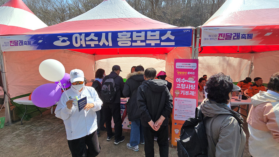 여수시 홍보부스에서 사람들이 축제 관련 정보를 얻고 있는 모습이다. 부스 앞에는 축제를 알리는 현수막과 배너가 설치되어 있다.