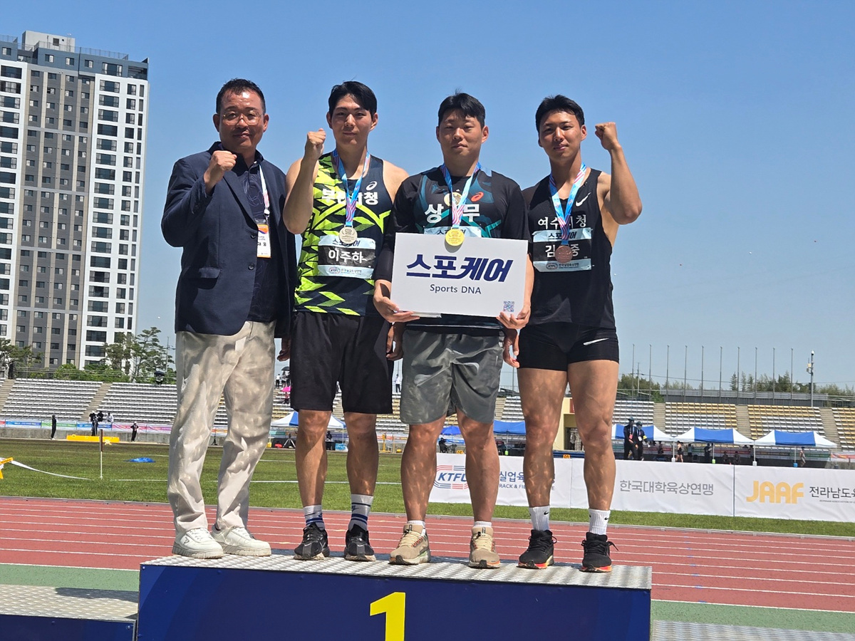 선수들이 메달을 목에 걸고 시상대에서 포즈를 취하고 있다. 한 선수가 스포츠 DNA라는 현수막을 들고 있다.