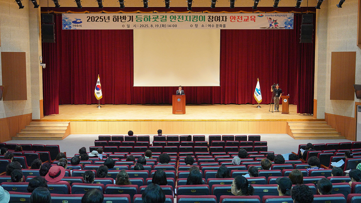 여수문화홀에서 2025년 하반기 등하굣길 안전지킴이 참여자를 위한 안전교육이 진행되고 있다. 강연자가 무대에서 교육을 하고 있으며, 청중이 앉아 있다.