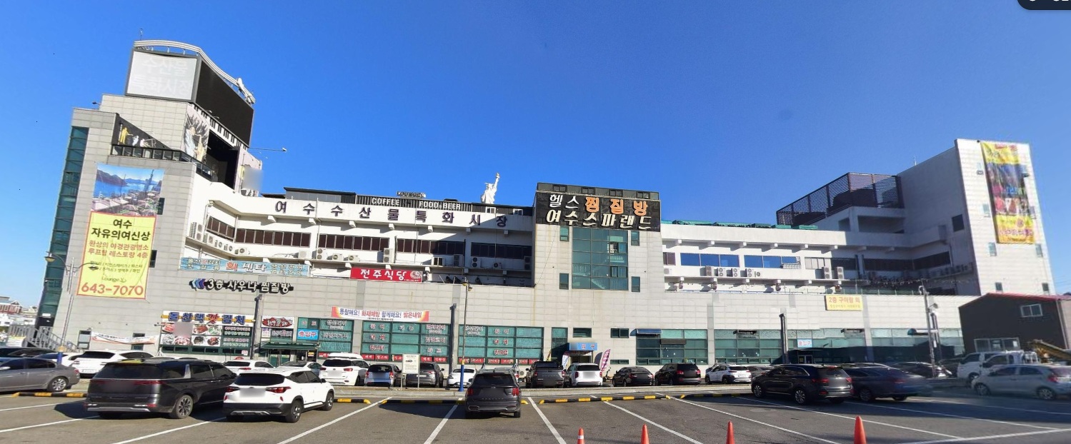 여수수산시장과 여수수산물특화시장이 보이는 외관으로, 주차장에 차량들이 주차되어 있다.