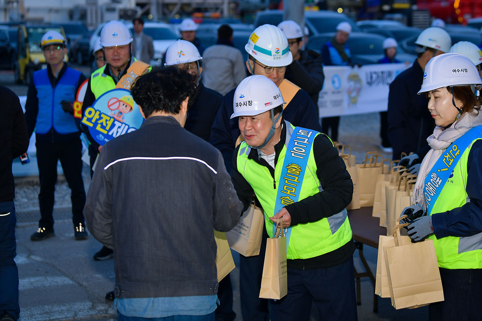 여수시 정기명 시장과 관계자들이 안전모와 형광 안전조끼를 착용하고 GS칼텍스 대정비 사업장 출근길에서 근로자들에게 안전 홍보물을 나눠주는 모습