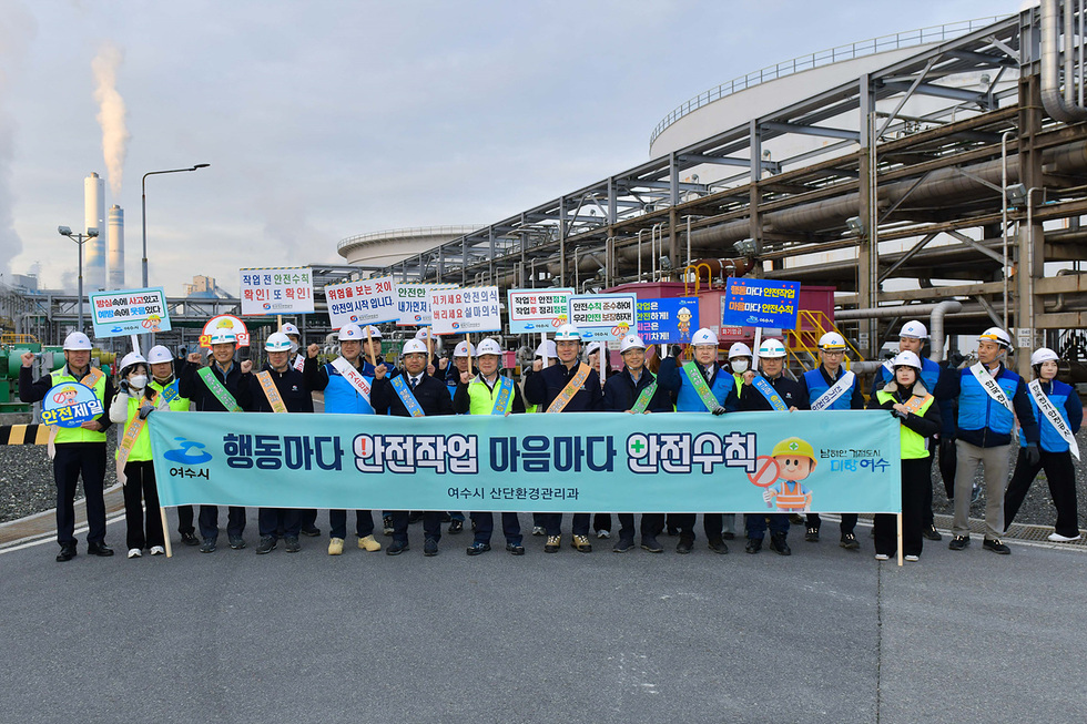 여수시에서 안전작업과 안전수칙을 홍보하는 행사에 참여한 사람들. 그들은 배너를 들고 있으며, 배경에는 산업 시설이 보인다.