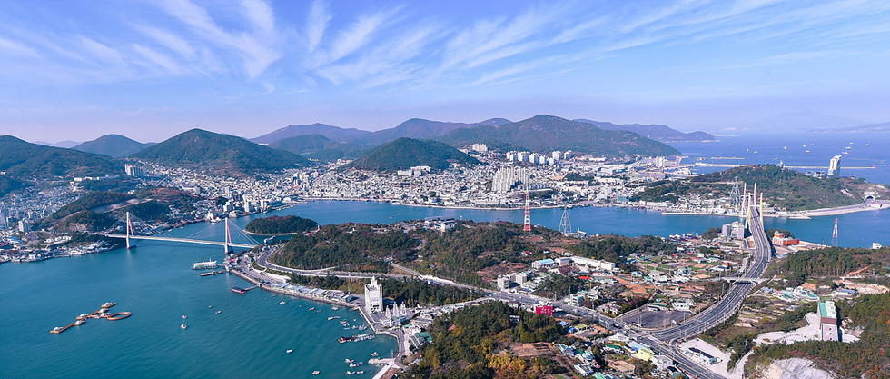 전경에서 바라본 해안 도시의 모습으로, 다리와 항구, 산이 어우러져 있다. 도시의 건물과 자연 경관이 조화를 이루고 있다.