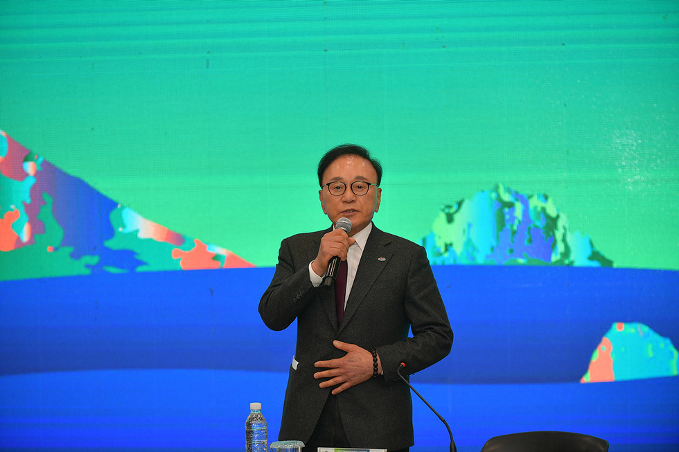 한 남성이 마이크를 들고 연설하고 있으며, 배경에는 다채로운 색상의 그래픽이 보인다.