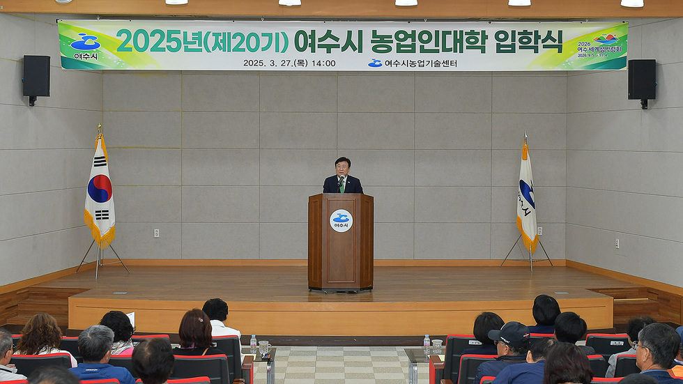 여수시 농업인대학 입학식에서 한 남성이 연단에서 발언하고 있으며, 청중이 그를 바라보고 있다.