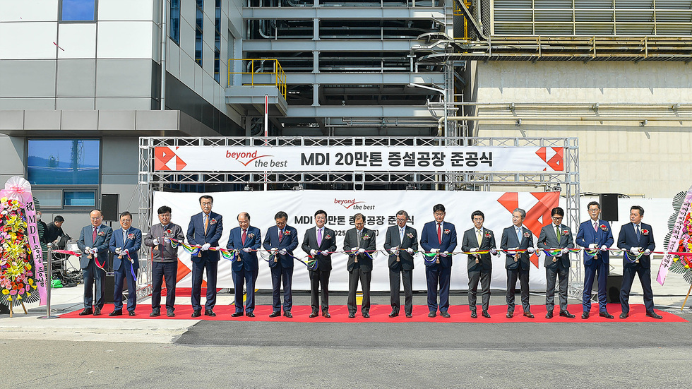 MDI 20만톤 증설공장 준공식에서 여러 명의 참석자들이 리본을 자르고 있다. 배경에는 현수막과 꽃다발이 보인다.