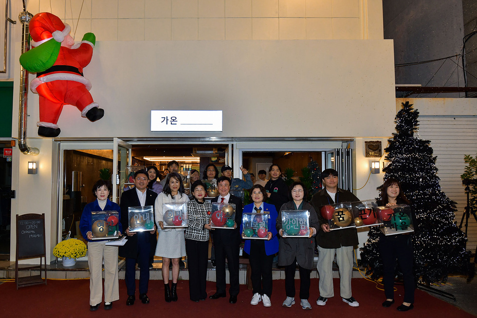 가온이라는 이름의 장소 앞에서 여러 사람들이 다양한 색상의 상자를 들고 서 있다. 상자에는 안내, 영업시간, 품목 등의 글자가 적혀 있다.