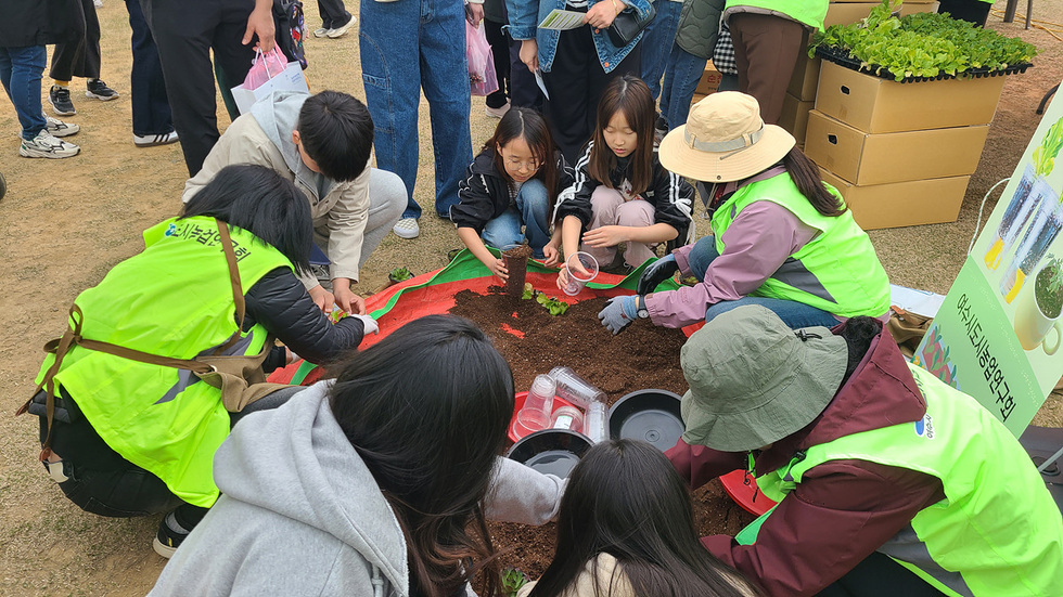 여주시농업기술센터에서 사람들이 모여 식물을 심고 있는 장면이다. 참가자들은 흙과 식물 모종을 사용하여 함께 작업하고 있다.