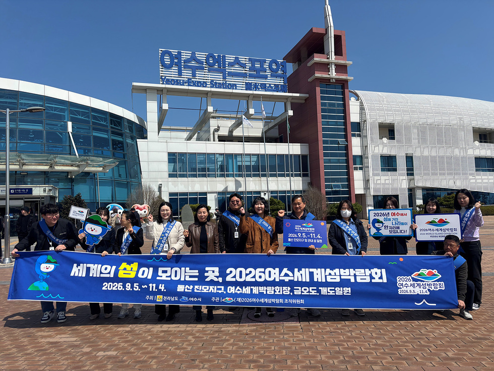 여수엑스포역 앞에서 2026수세미세계섬박람회를 홍보하는 사람들. 배너에는 박람회 일정과 주최, 주관 정보가 적혀 있다.