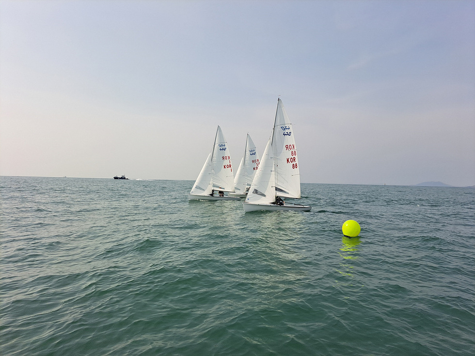 세 척의 요트가 바다에서 경주하고 있으며, 노란 부표가 가까이에 떠 있다.