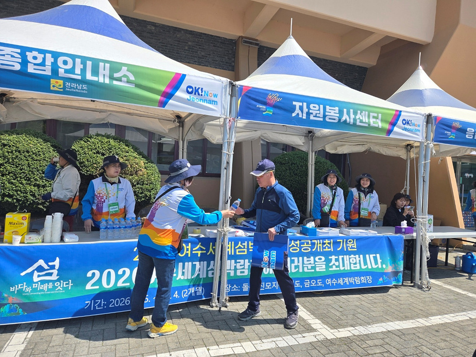 여수세계박람회 2023을 지원하는 자원봉사자들이 종합안내소에서 방문객에게 음료를 제공하고 있는 장면이다.