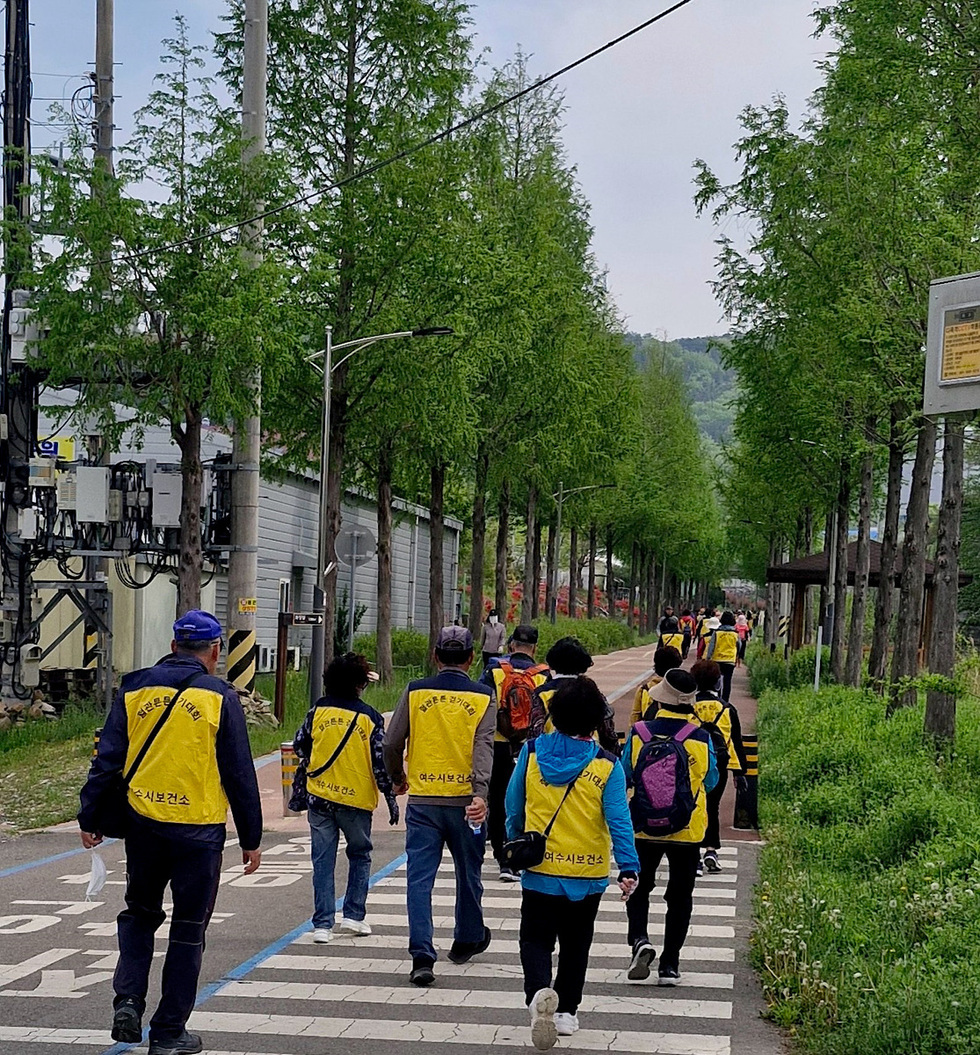 여수에서 안전한 도시 만들기를 위한 활동에 참여하는 사람들이 노란 조끼를 입고 도로를 걷고 있다.