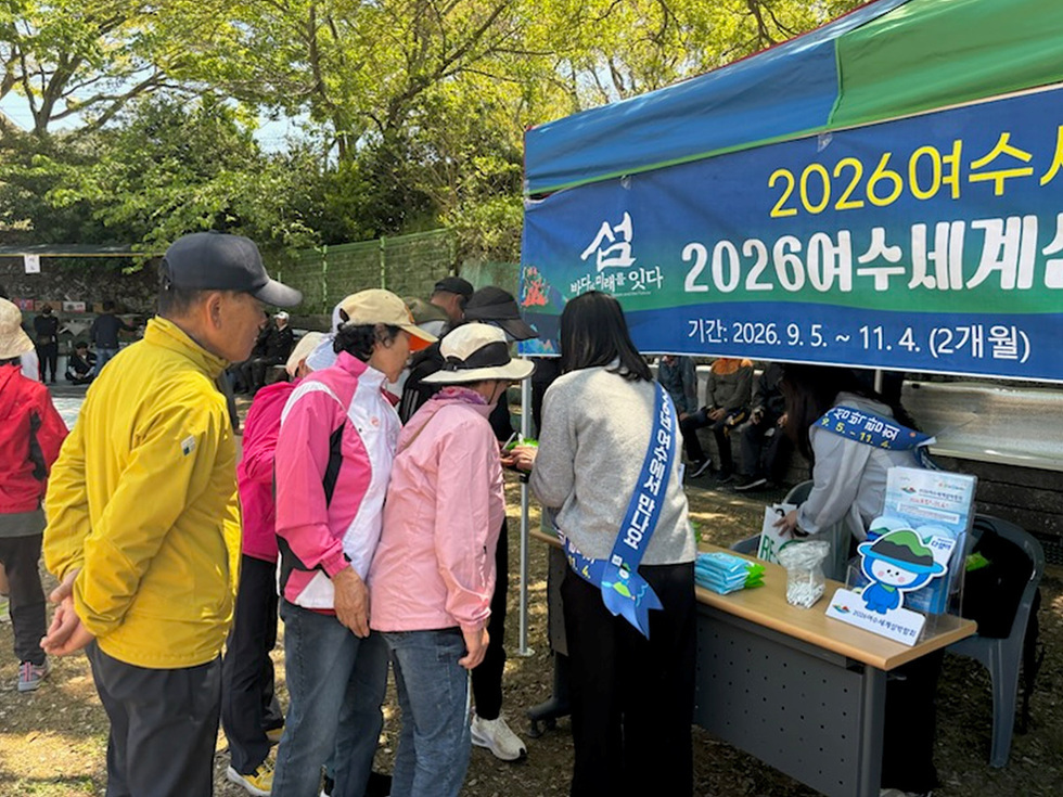 2026여수세계섬 행사에 참여하기 위해 사람들이 부스에 모여 있는 모습으로, 부스에는 행사 기간과 관련된 정보가 적혀 있다.