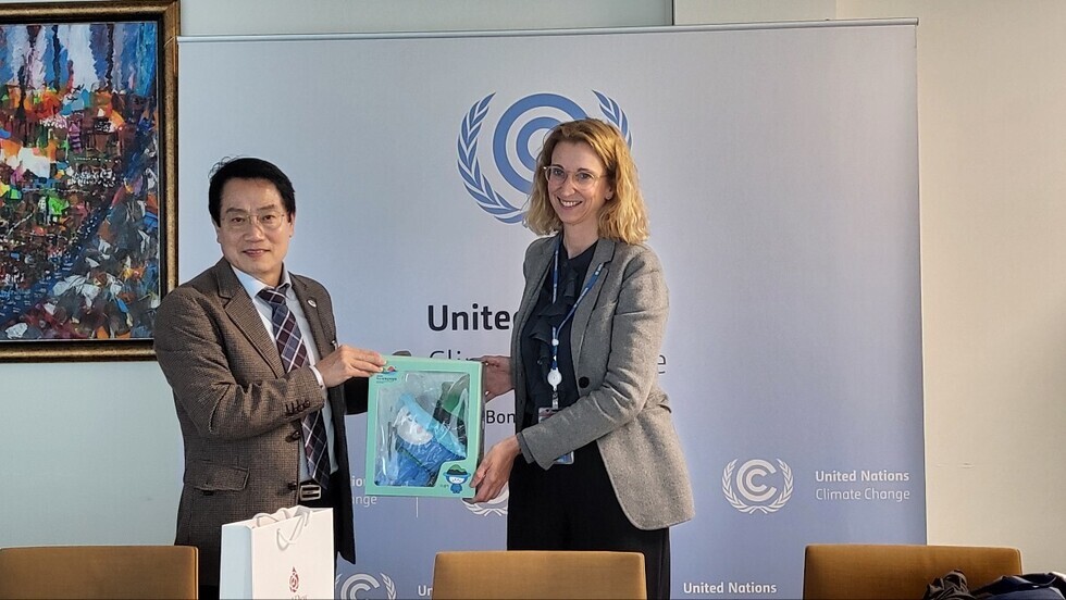 두 사람이 유엔 기후 변화 배경 앞에서 선물 상자를 교환하고 있다.