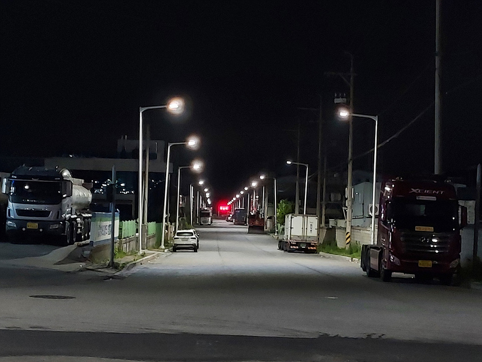 어두운 밤에 도로에 여러 대의 트럭과 차량이 주차되어 있는 모습이다. 도로 양쪽에 가로등이 켜져 있다.