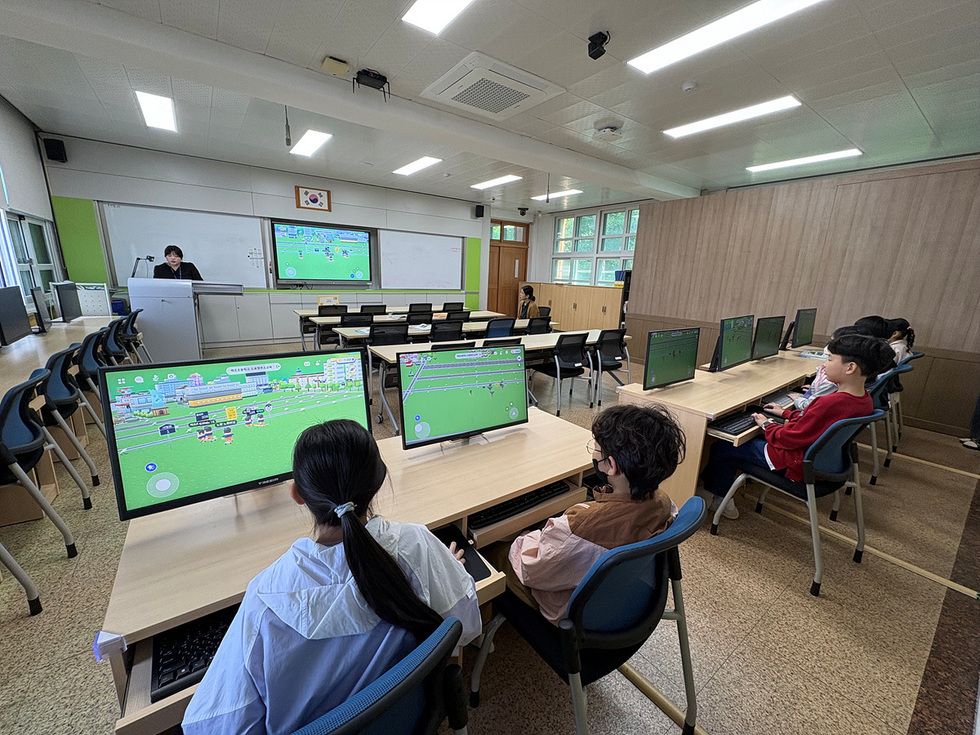 교실에서 학생들이 컴퓨터 앞에 앉아 게임을 하고 있으며, 강사가 강의 중이다. 화면에는 게임 화면이 표시되고 있다.