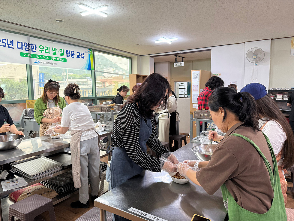 여러 사람이 요리 교실에서 쌀과 밀을 활용한 요리를 배우고 있는 모습이다. 교육생들이 재료를 손질하고 요리를 준비하고 있다.