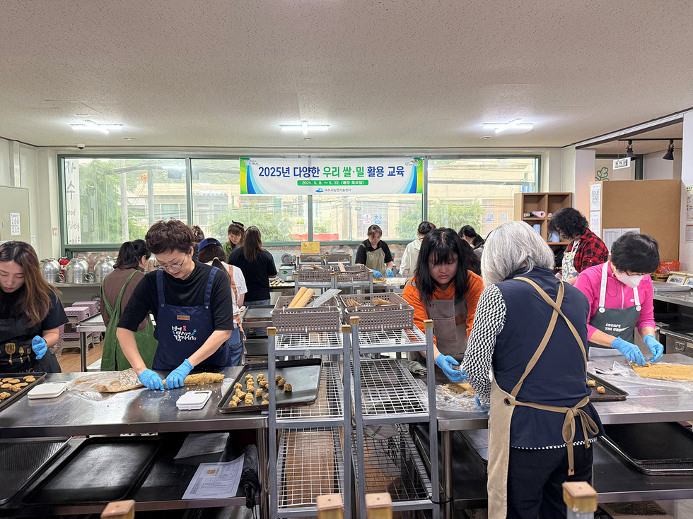여러 사람이 교육 공간에서 우리밀을 활용한 요리를 하고 있는 모습이다. 교육 배너가 보인다.