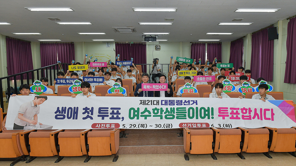 여수의 한 교실에서 학생들이 제21대 대통령선거를 위한 첫 투표를 독려하는 모습이다. 학생들이 다양한 피켓을 들고 있으며, 현수막에는 사전투표와 선거일에 대한 정보가 적혀 있다.