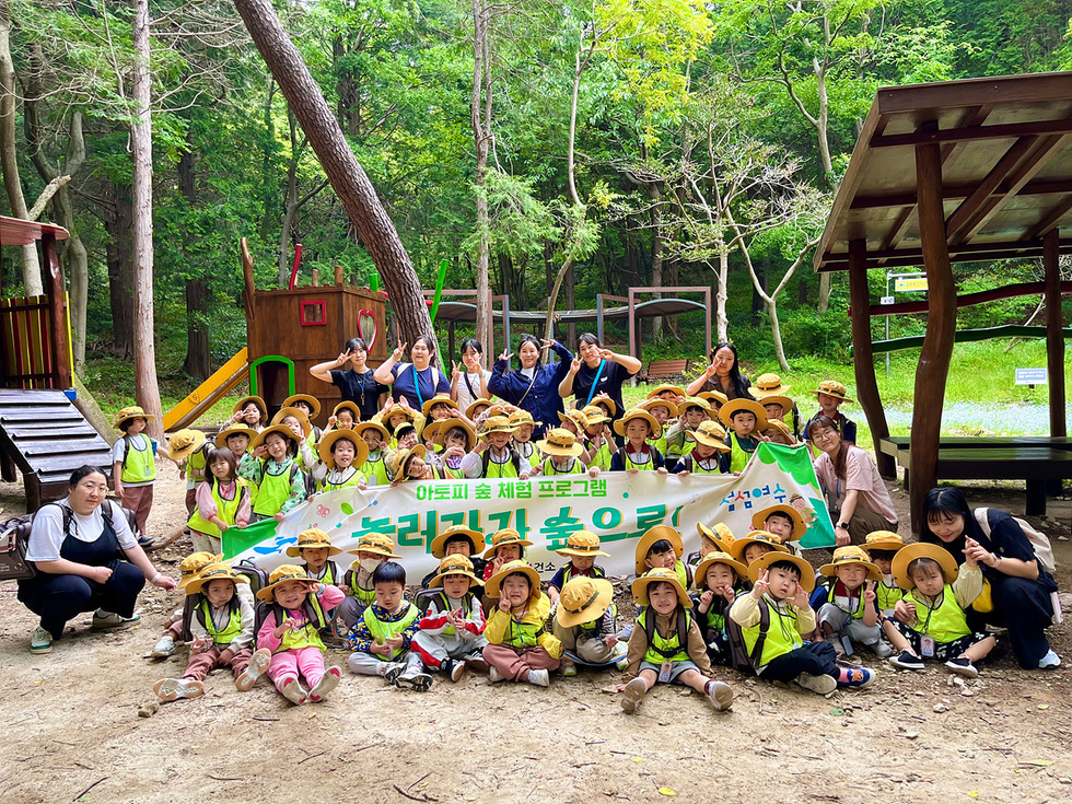 아이들과 교사들이 숲속에서 아토피 숲 체험 프로그램에 참여하며 단체 사진을 찍고 있다.