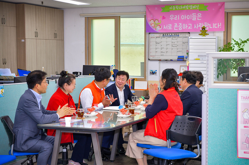 회의실에서 여러 사람이 모여 아동학대 예방 캠페인에 대해 논의하고 있다. 배경에는 캠페인 슬로건이 적힌 현수막이 걸려 있다.