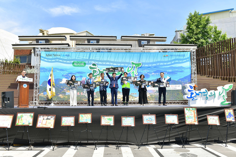 제30회 환경의 날 기념 행사에서 여러 사람이 기념 사진을 들고 서 있다. 배경에는 환경을 주제로 한 그림들이 전시되어 있다.