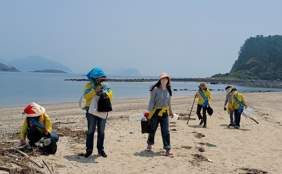 여수시 문화관광해설사들이 사도 해변에서 쓰레기를 주우며 환경정화 활동을 하는 모습, 모자와 장비를 착용하고 바닷가 플로깅 봉사 참여