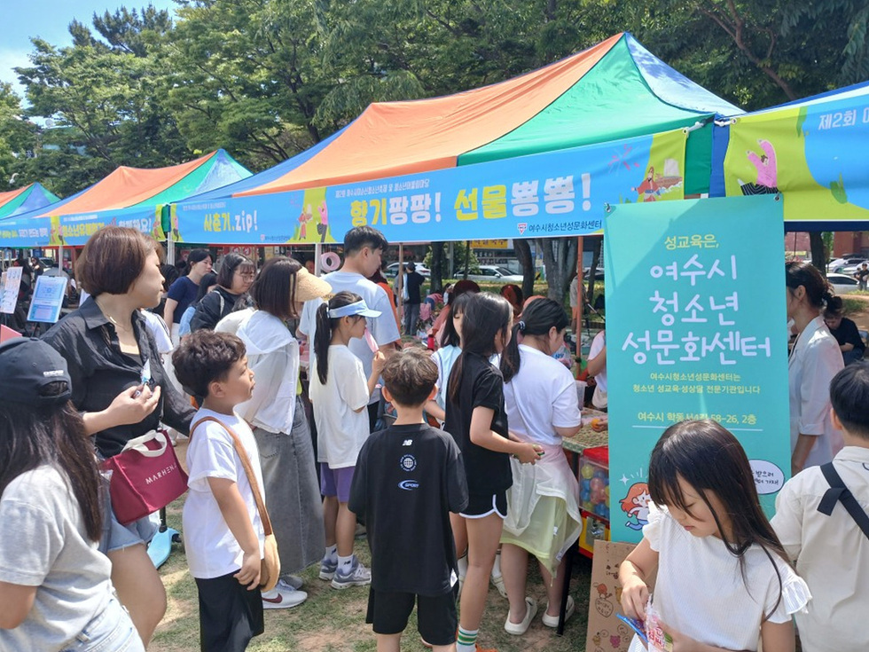 여수시 청소년 성문화센터 부스에서 사람들이 다양한 활동을 하고 있는 모습이다. 부스에는 청소년 성교육 관련 정보가 게시되어 있다.