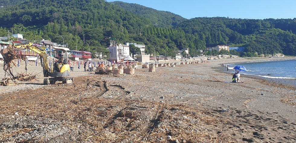 중장비와 작업 인력이 해수욕장 모래사장에서 해양쓰레기를 수거하고 정리하는 장면
