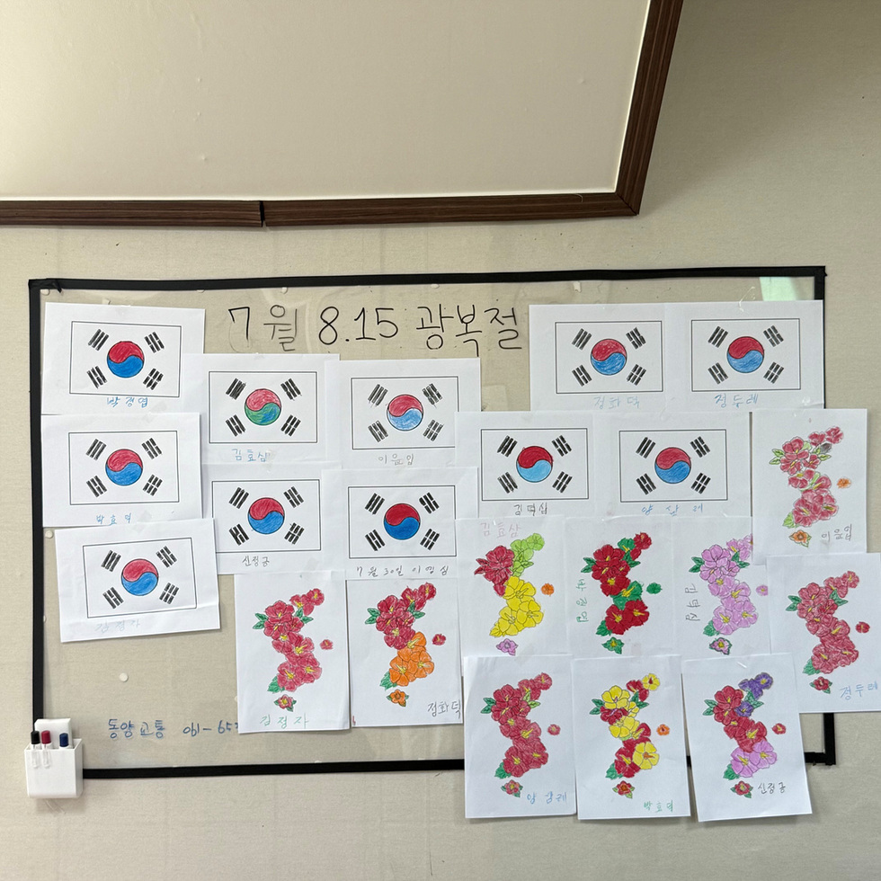 7월 8.15 광복절’이라는 제목 아래 태극기 색칠 그림과 무궁화 그림이 벽에 전시되어 있음. 어르신들이 직접 참여한 문해교육 결과물