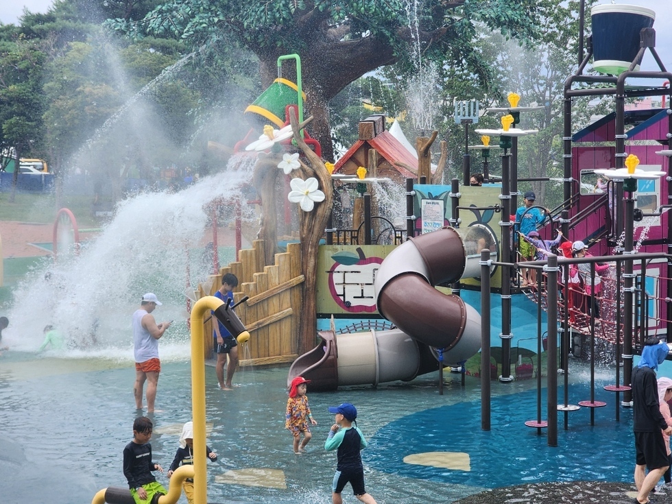 어린이들이 물놀이를 즐기는 워터파크의 모습으로, 다양한 놀이시설과 물줄기가 있는 장면이다.