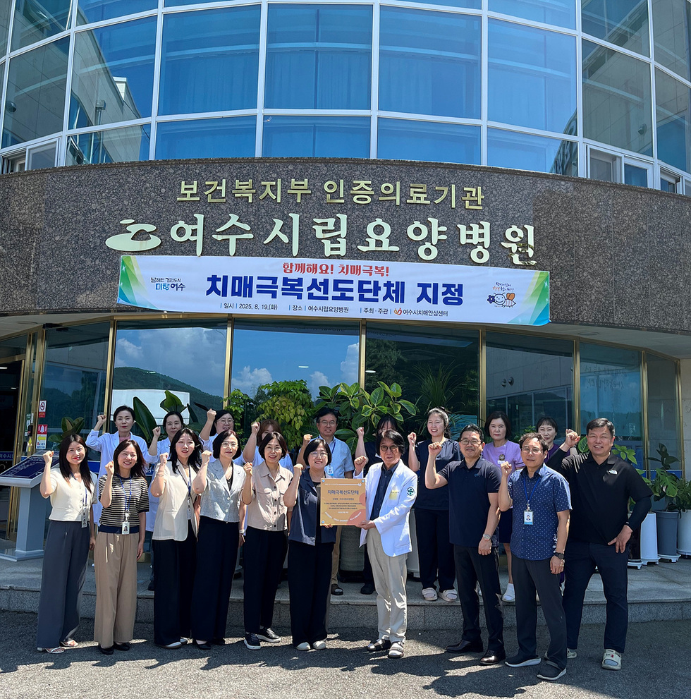 여수시립요양병원 앞에서 여러 사람들이 치매극복선도단체 지정을 축하하며 기념사진을 찍고 있다.