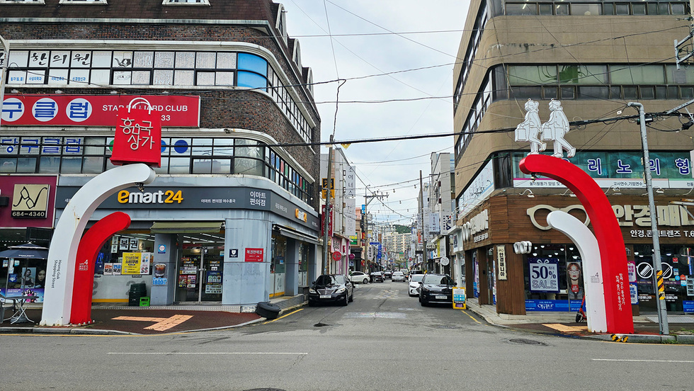 흥국 상가 입구에 위치한 e마트24 편의점과 50% 세일을 알리는 간판이 보이는 거리 풍경