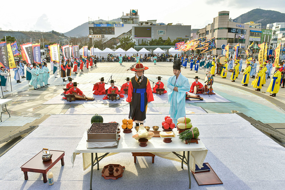 제주도민속예술축제에서 전통 의상을 입은 사람들이 제단 앞에서 제사를 지내고 있다. 배경에는 관중과 여러 전통 공연팀이 보인다.