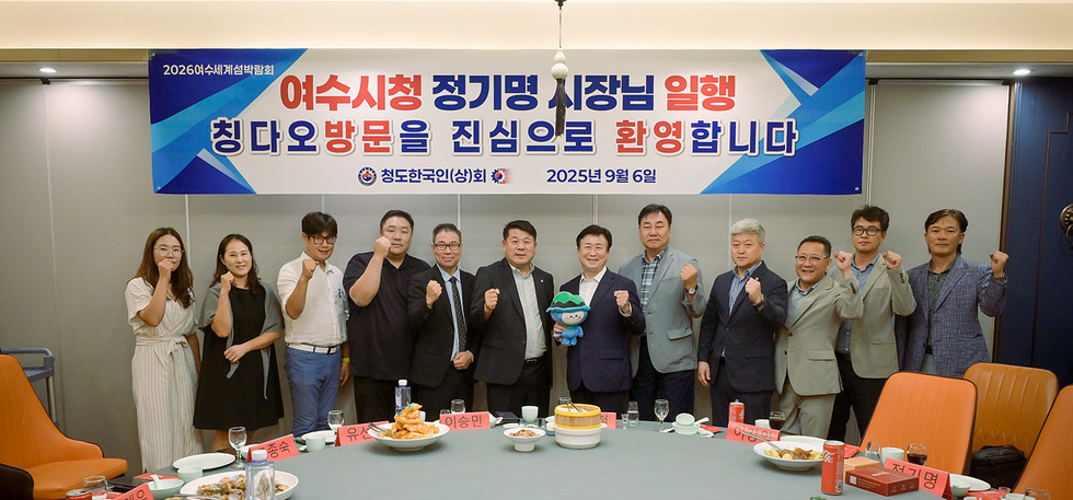 여수시장 정기명과 일행이 칭다오 방문을 환영하는 행사에서 포즈를 취하고 있다. 배경에는 환영 메시지가 적힌 현수막이 걸려 있다.