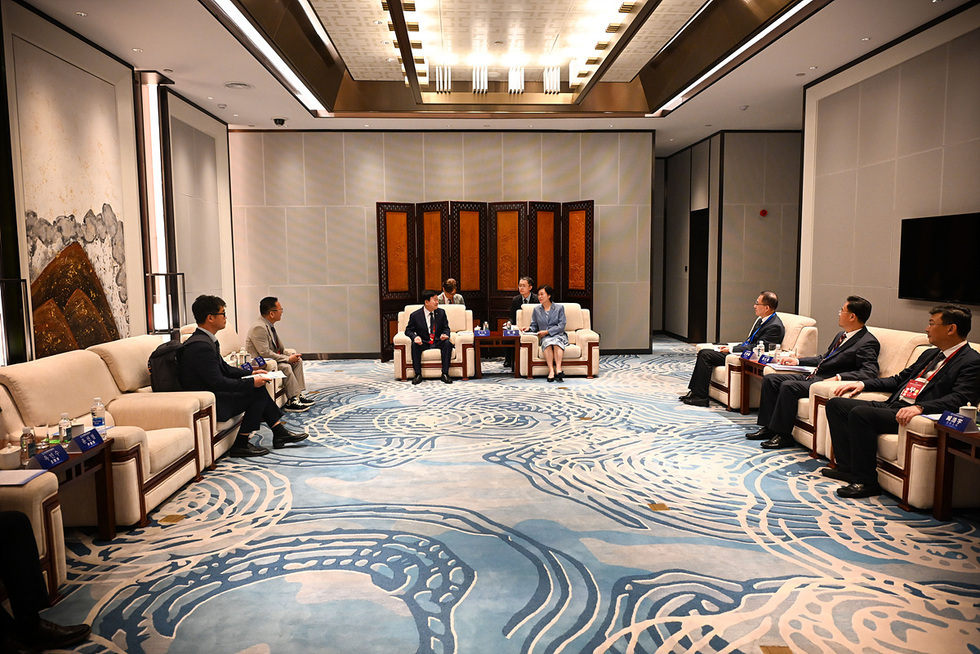 회의실에서 여러 명의 사람들이 앉아 대화를 나누고 있는 모습이다. 중앙에 있는 두 사람은 서로 마주 보며 대화하고 있으며, 주변에 다른 참석자들이 앉아 있다.