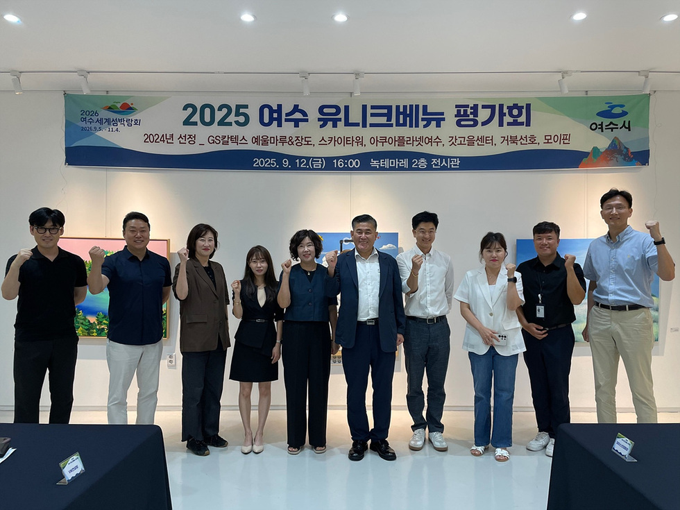 2025 여수 유니크베뉴 평가회에서 관계자들이 전시관 앞에 함께 서서 기념촬영을 하며 주먹을 쥐어 올려 파이팅 포즈를 취하는 모습, 행사 성과 공유와 향후 활성화를 논의하는 자리임을 보여줌