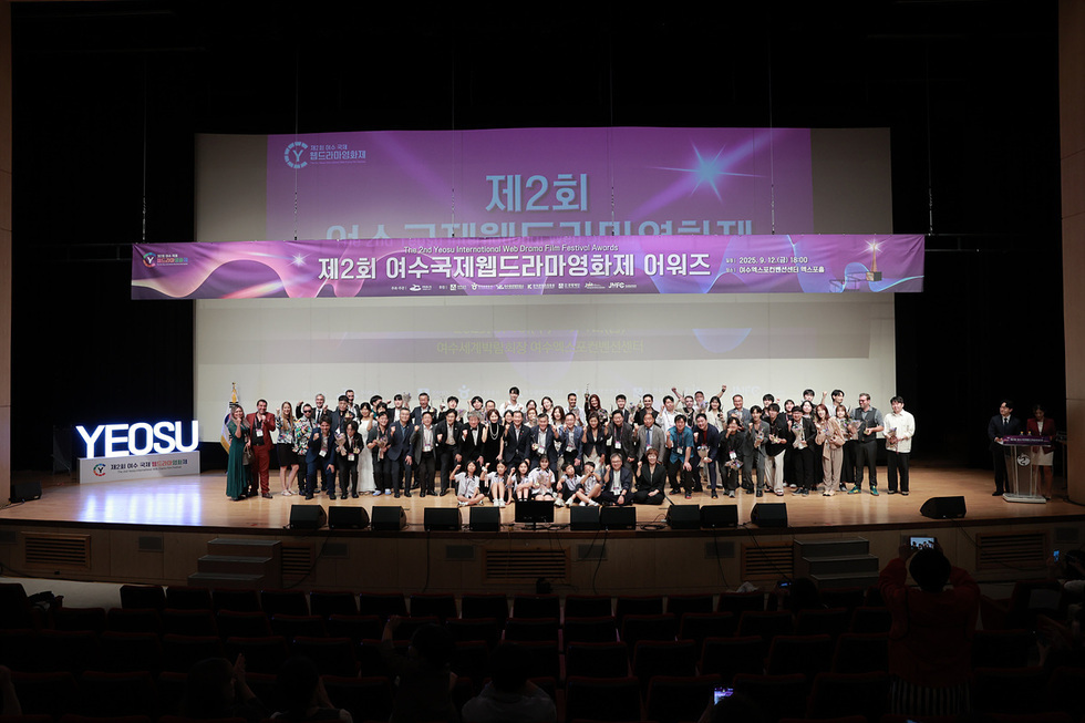 정기명 여수시장과 독일·스페인 대표가 무대 위에서 업무협약서를 들고 함께 기념촬영을 하는 모습, 여수가 글로벌 웹콘텐츠 허브 도약을 위해 해외 페스티벌과 협약을 체결함을 보여줌.