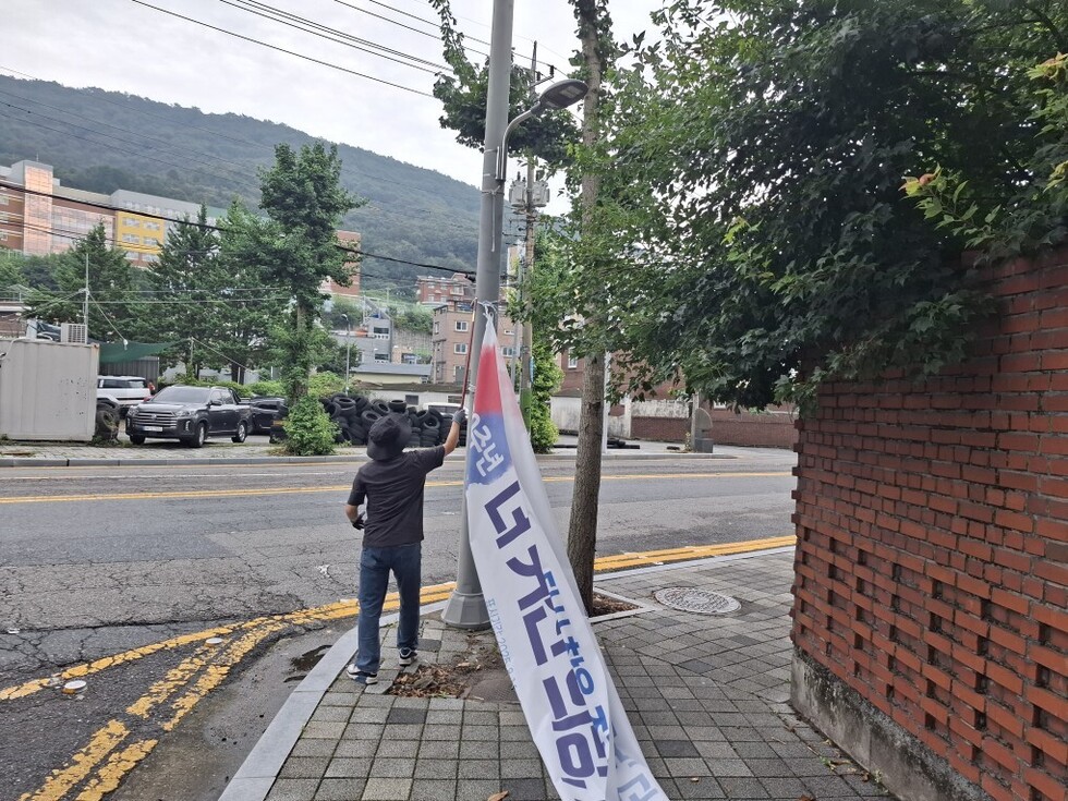 여수시 불법 현수막 정비 활동 모습, 작업자가 가로등 기둥에 설치된 현수막을 철거하는 장면