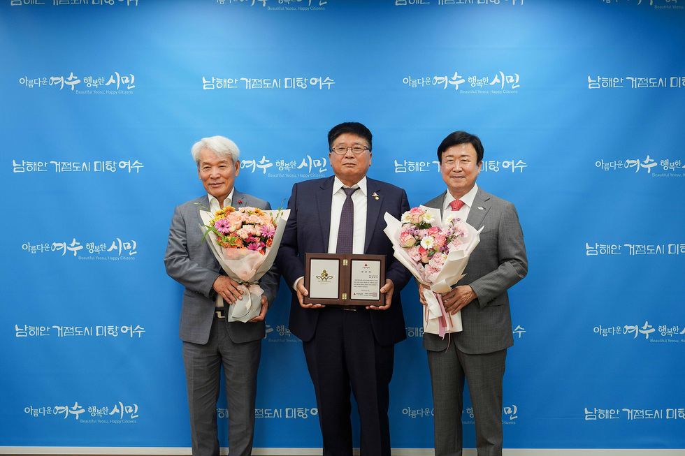 여수시장에서 황태식 대표가 아너 소사이어티 회원 가입을 축하받고 있는 장면으로, 참석자들이 꽃다발을 들고 기념 촬영을 하고 있다.