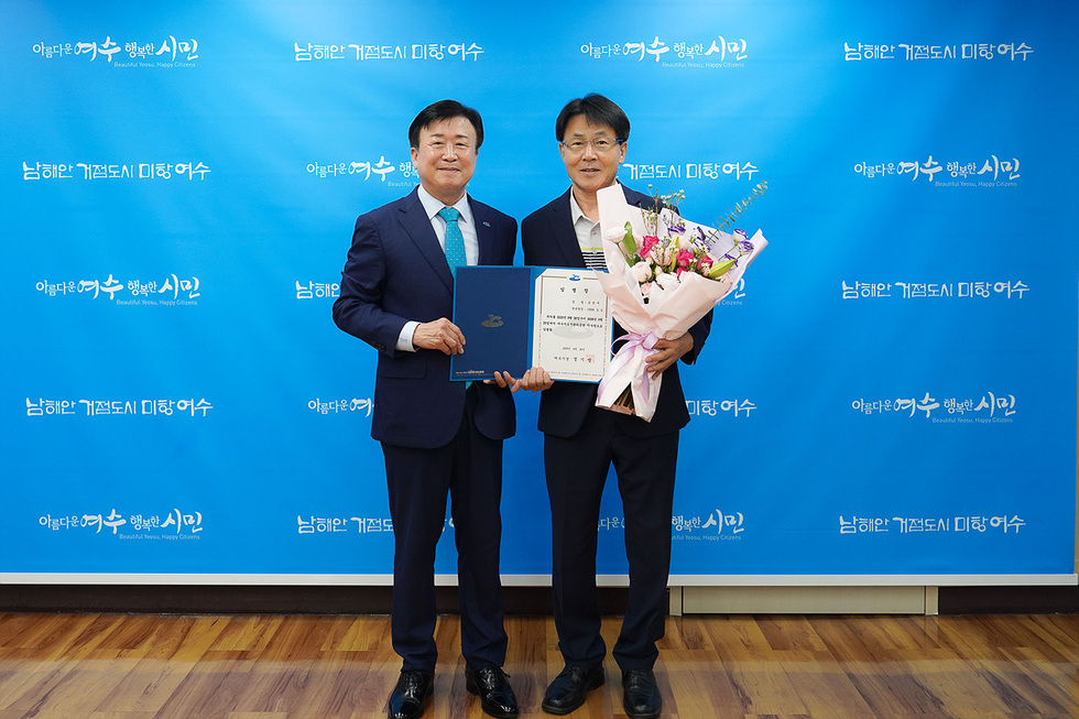 여수시 정기명 시장이 송병구 이사장에게 임명장을 수여하며 기념촬영을 하고 있다. 배경에는 여수시의 나해안 거점도시 미항여수 슬로건이 적힌 현수막이 있다.