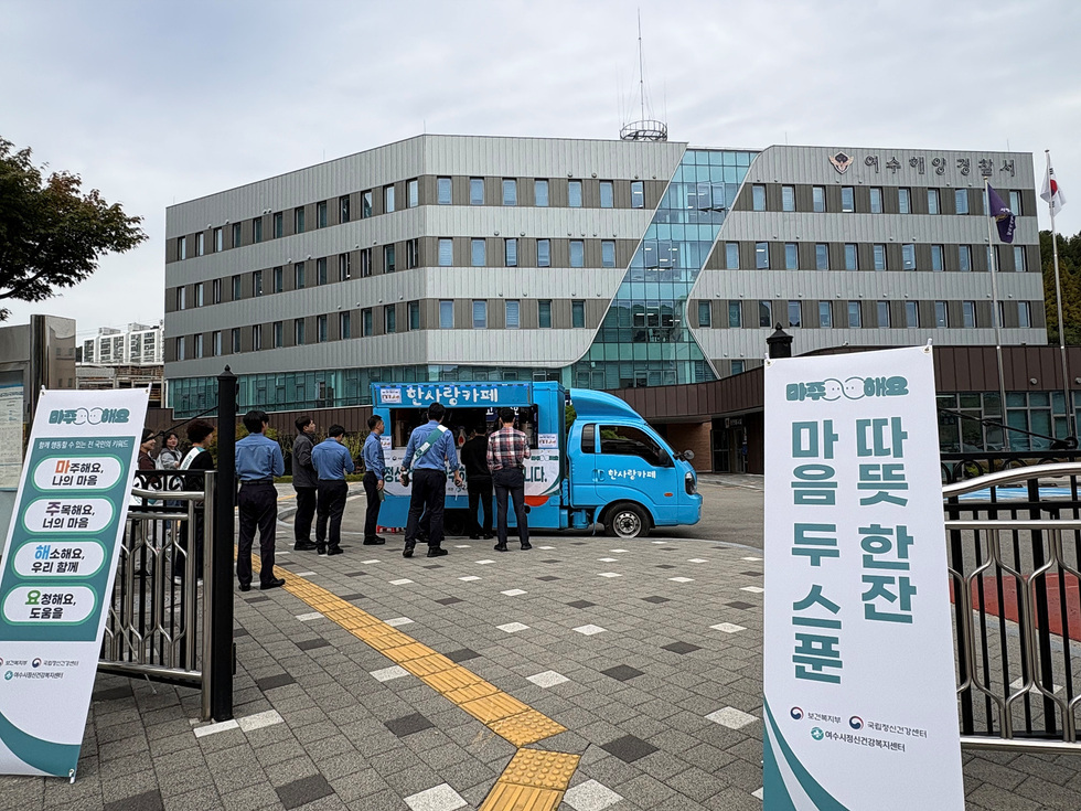 여수해양경찰서 앞에서 시민들이 커피차 캠페인에 참여하고 있으며, 정신건강 홍보 메시지가 적힌 현수막이 보인다.