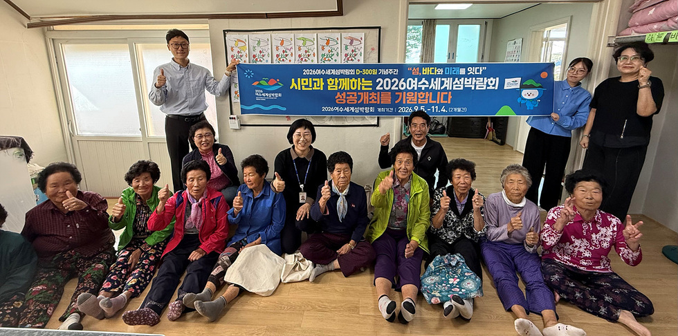 여수시 화양면 이목마을회관에서 어르신들과 함께 2026여수세계섬박람회를 응원하는 장면으로, 참여단원들이 현수막을 들고 있다.