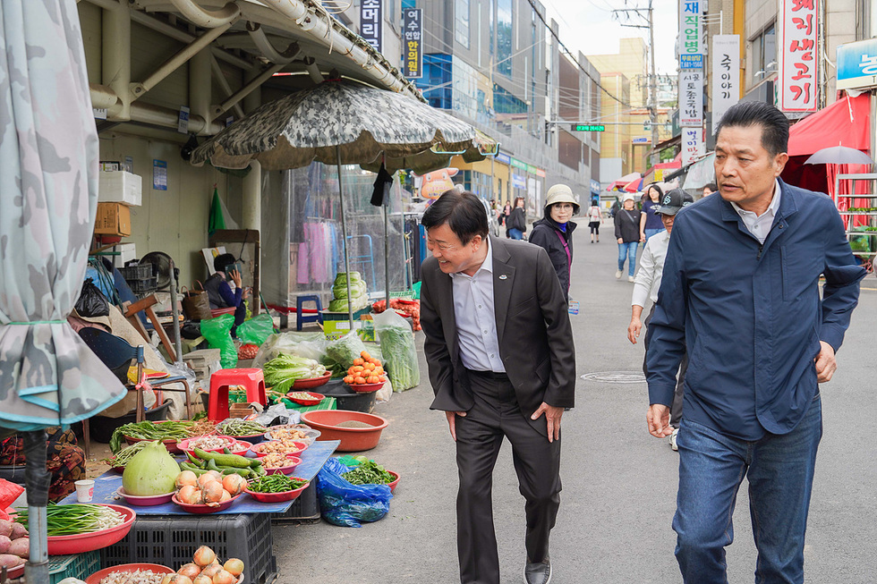 정기명 여수시장이 진남시장에서 상인과 대화하며 시장을 둘러보고 있다. 시장에는 다양한 채소와 과일이 진열되어 있다.