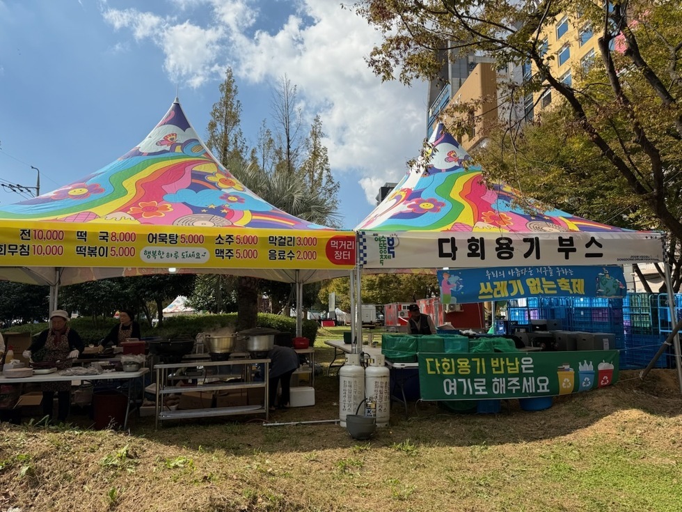 여수동동북축제에서 다회용기 부스가 설치되어 있으며, 다양한 음식과 음료의 가격이 표시되어 있다. 부스에는 다회용기 반납 안내문이 부착되어 있다.