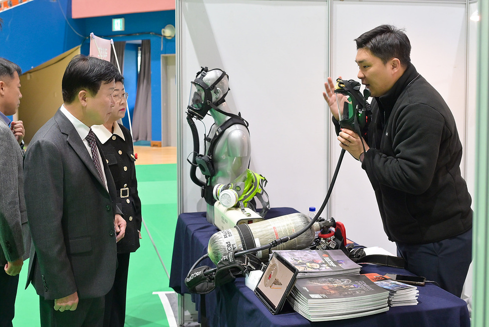 안전장비를 설명하는 참가자와 이를 듣고 있는 평가자들이 있는 장면으로 재난 대응을 위한 평가로 보인다.