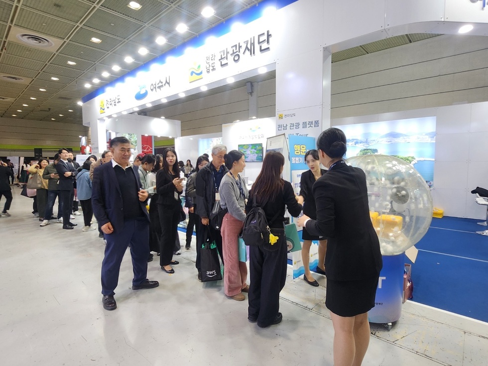 코엑스 ‘전남관광재단’ 홍보부스 앞에서 관람객들이 줄을 서서 ‘행운의 볼돌리기 이벤트’에 참여하며 직원의 안내를 받는 모습